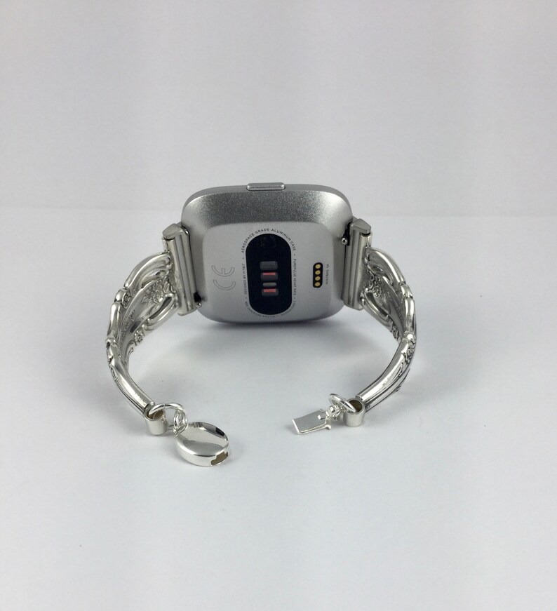 May include: Silver smartwatch with a silver, ornate, bracelet-style band. The watch face is black and displays the text "CE" and "MADE IN TAIWAN".