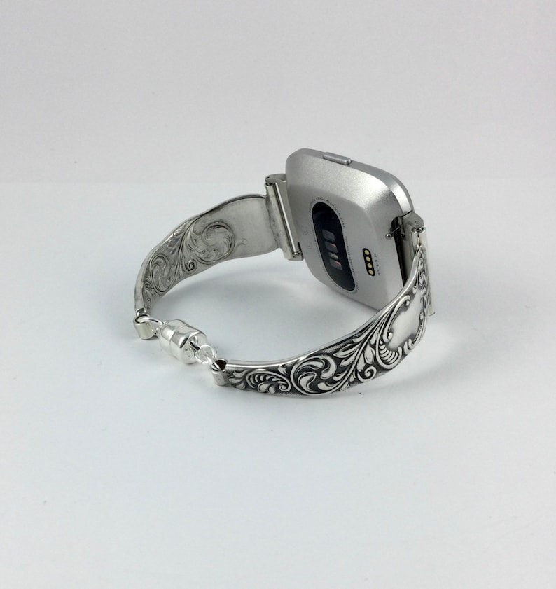 Puede incluir: Pulsera de reloj de plata con un dise&ntilde;o floral adornado. La pulsera est&aacute; hecha para adaptarse a un reloj inteligente de forma cuadrada.