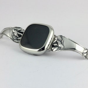 Peut inclure: Un bracelet de montre argent&eacute; avec un motif floral. Le cadran de la montre est noir et de forme carr&eacute;e.