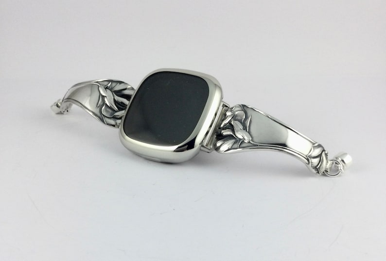 Peut inclure: Un bracelet de montre argent&eacute; avec un motif floral. Le cadran de la montre est noir et de forme carr&eacute;e.