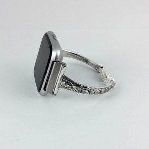 May include: A silver smartwatch with a black screen is attached to a silver bracelet with an ornate floral design.