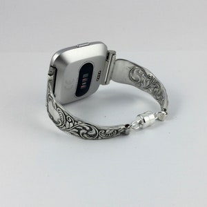 Puede incluir: Pulsera de reloj de plata con un dise&ntilde;o floral adornado. La pulsera est&aacute; hecha para adaptarse a un reloj inteligente de forma cuadrada.
