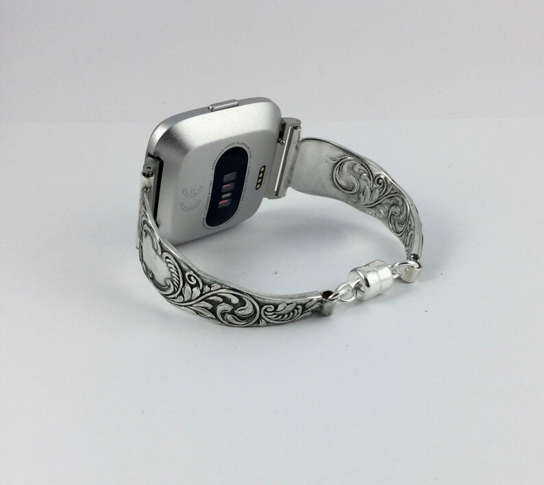Puede incluir: Pulsera de reloj de plata con un dise&ntilde;o floral adornado. La pulsera est&aacute; hecha para adaptarse a un reloj inteligente de forma cuadrada.