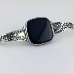 May include: Silver watch strap with a square black face. The strap has detailed floral and scrollwork patterns. The watch is shown against a white backdrop.