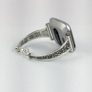 Puede incluir: Pulsera de reloj de plata con dise&ntilde;o floral. La pulsera est&aacute; unida a un reloj inteligente plateado.