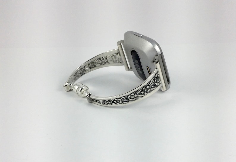 Puede incluir: Pulsera de reloj de plata con dise&ntilde;o floral. La pulsera est&aacute; unida a un reloj inteligente plateado.