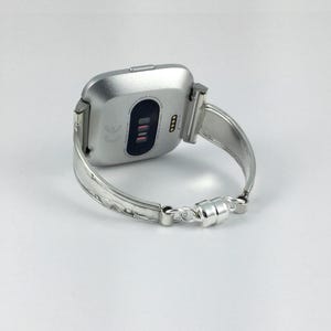 Peut inclure: Un bracelet de montre en m&eacute;tal argent&eacute; avec un cadran de montre carr&eacute; argent&eacute;. Le cadran de la montre a un &eacute;cran noir avec un petit logo blanc et une rang&eacute;e de quatre lumi&egrave;res rouges.