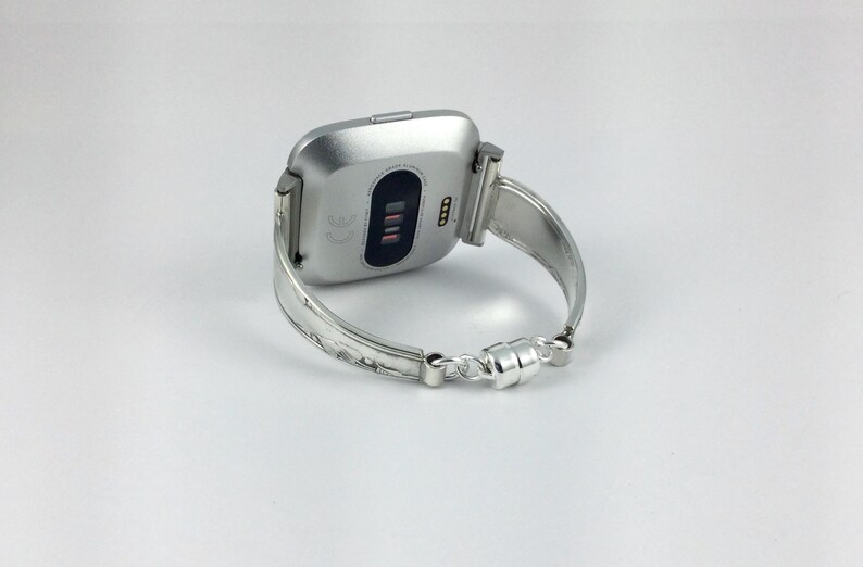 Peut inclure: Un bracelet de montre en m&eacute;tal argent&eacute; avec un cadran de montre carr&eacute; argent&eacute;. Le cadran de la montre a un &eacute;cran noir avec un petit logo blanc et une rang&eacute;e de quatre lumi&egrave;res rouges.
