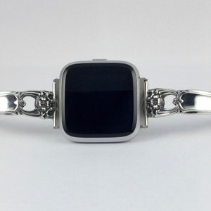 May include: A silver watch band made from a repurposed silverware piece. The band is attached to a square-shaped smartwatch with a black screen.