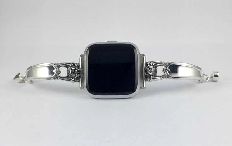 May include: A silver watch band made from a repurposed silverware piece. The band is attached to a square-shaped smartwatch with a black screen.