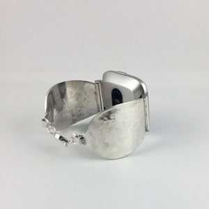 May include: A silver watch with a hammered metal band. The watch face is square and has a silver finish.