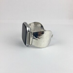May include: A silver watch band with a hammered metal design. The band is curved and has a silver watch face attached.