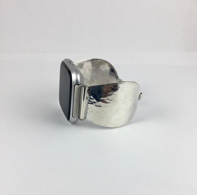 May include: A silver watch band with a hammered metal design. The band is curved and has a silver watch face attached.