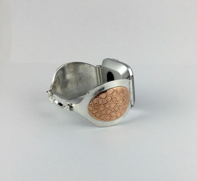 May include: A silver bracelet with a copper-coloured oval design. The bracelet is open and has a hinge on one side.