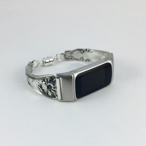 May include: A silver-toned bracelet with a rectangular black screen. The bracelet is made from repurposed silverware, featuring floral and ornate designs. The clasp is magnetic. The watch face is approximately 1.5 inches long.
