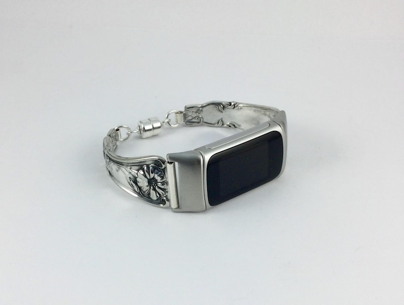 May include: A silver-toned bracelet with a rectangular black screen. The bracelet is made from repurposed silverware, featuring floral and ornate designs. The clasp is magnetic. The watch face is approximately 1.5 inches long.