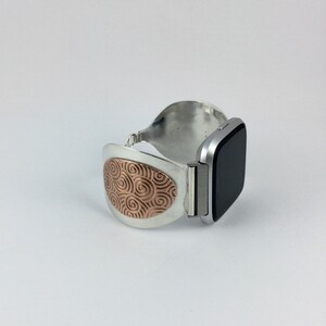 May include: A silver and rose gold watch band with a swirl pattern on the band. The band is designed to fit a square-shaped smartwatch.