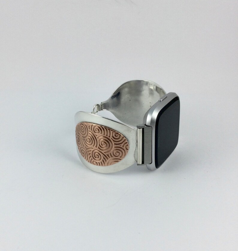 May include: A silver and rose gold watch band with a swirl pattern on the band. The band is designed to fit a square-shaped smartwatch.
