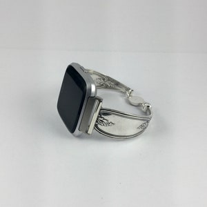 May include: A silver smartwatch with a black screen is attached to a silver bracelet made from a repurposed spoon.