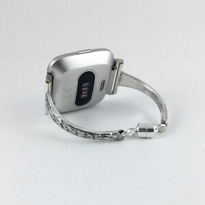 May include: Silver smartwatch with a textured silver band. The band has a magnetic clasp.