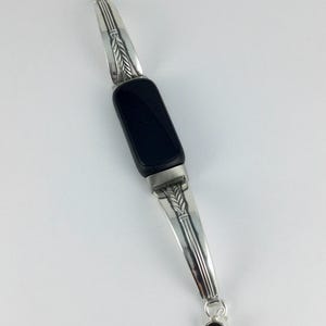 May include: A silver bracelet with a rectangular black stone center. The silver sections have a wheat stalk design. The bracelet has a small black stone at the clasp. The bracelet is shown on a white background.