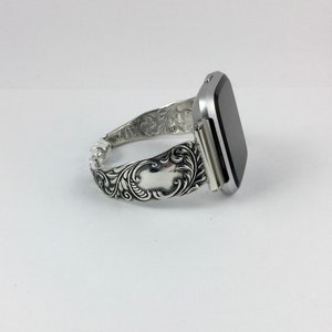 Puede incluir: Una pulsera de reloj plateada con un dise&ntilde;o floral adornado. La pulsera est&aacute; hecha de metal y tiene un acabado pulido.