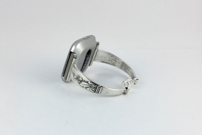Op de afbeelding: Een zilveren horloge met een vierkante wijzerplaat en een zilveren armband. De armband heeft een sierlijk ontwerp.