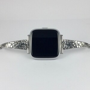 May include: A silver smartwatch with a black screen and a silver band with an intricate floral design.