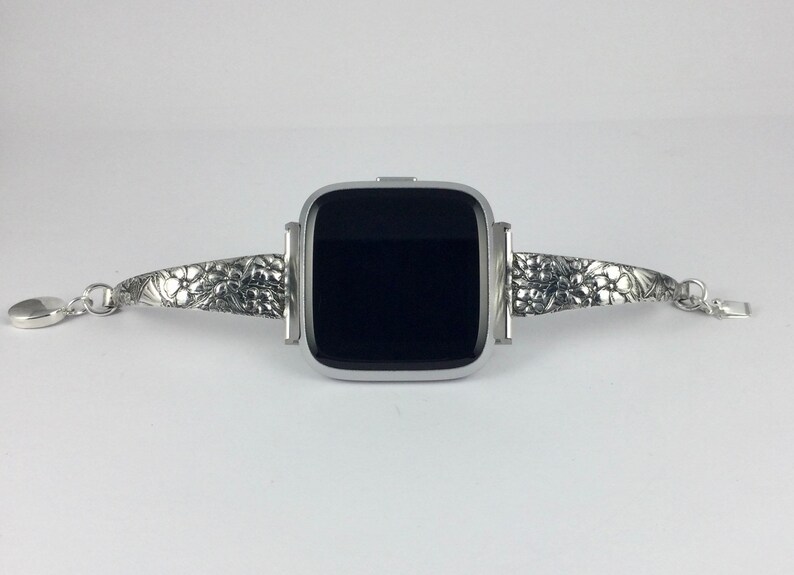 May include: A silver smartwatch with a black screen and a silver band with an intricate floral design.