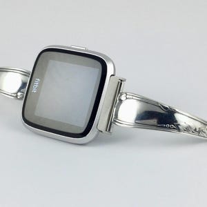 Peut inclure: Une montre intelligente Fitbit argent&eacute;e fix&eacute;e &agrave; un bracelet argent&eacute; fabriqu&eacute; &agrave; partir d'une cuill&egrave;re r&eacute;utilis&eacute;e.