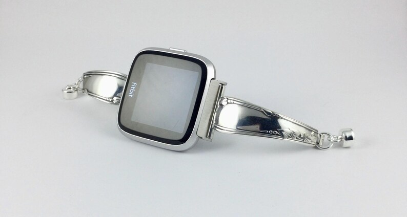 Peut inclure: Une montre intelligente Fitbit argent&eacute;e fix&eacute;e &agrave; un bracelet argent&eacute; fabriqu&eacute; &agrave; partir d'une cuill&egrave;re r&eacute;utilis&eacute;e.