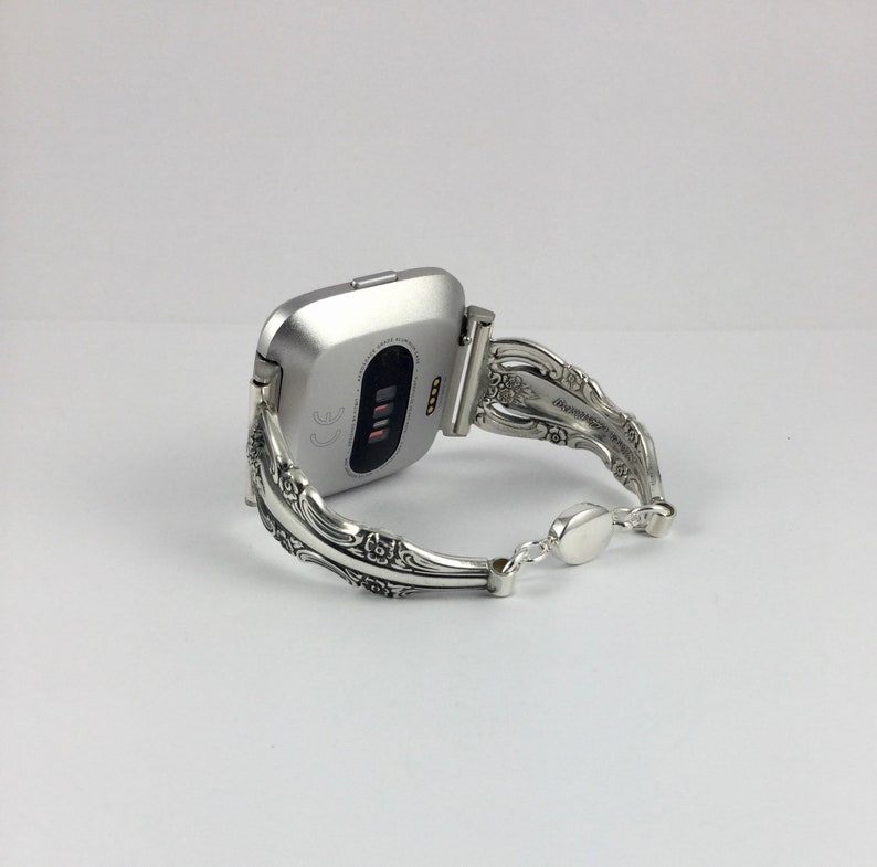 May include: Silver-toned fitness tracker with a silver, ornate, spoon-style watch band.