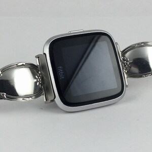 May include: A silver Fitbit smartwatch with a custom-made band made from a repurposed silverware spoon.