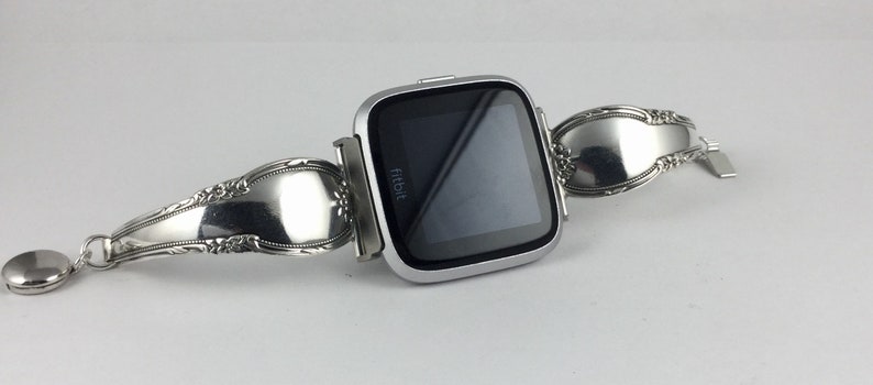 May include: A silver Fitbit smartwatch with a custom-made band made from a repurposed silverware spoon.