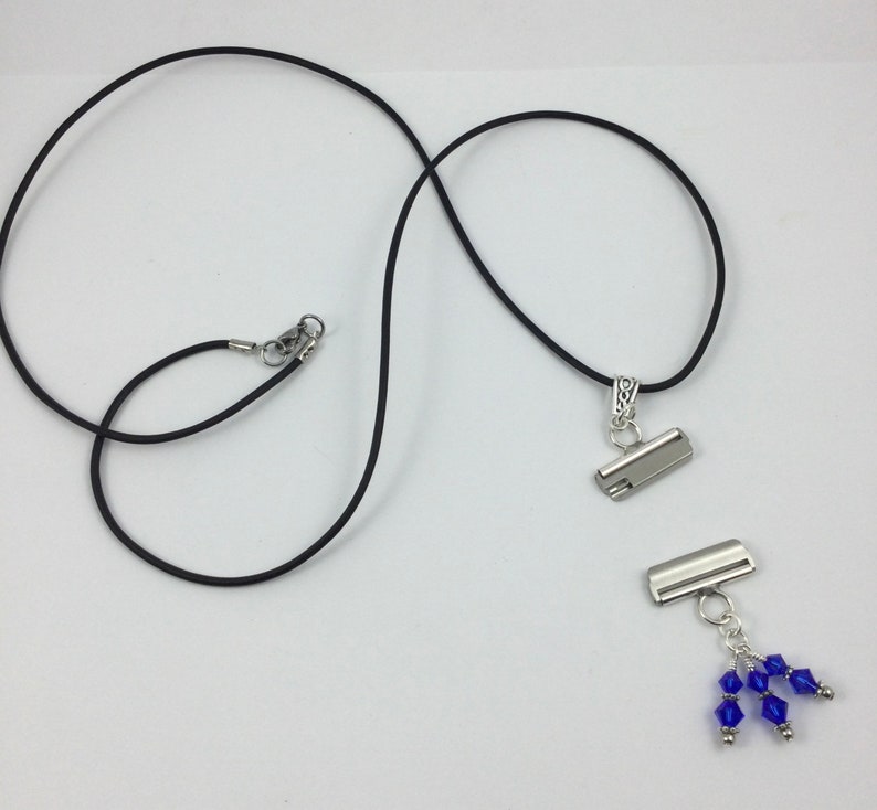 May include: A black cord necklace with a silver-colored clasp and pendant. The pendant has a silver-colored metal clasp with a cluster of blue crystal beads. The necklace is displayed on a white background.