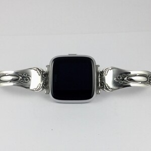May include: A silver smartwatch with a black screen is attached to a silver bracelet made from two vintage silverware spoons.