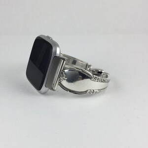 May include: A silver smartwatch with a black screen is attached to a silver spoon bracelet.