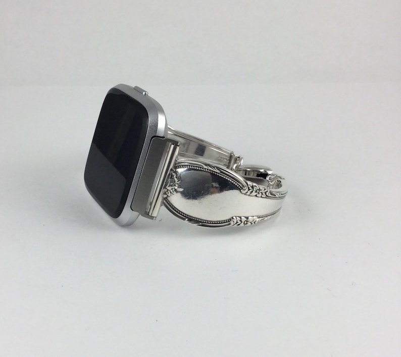 May include: A silver smartwatch with a black screen is attached to a silver spoon bracelet.