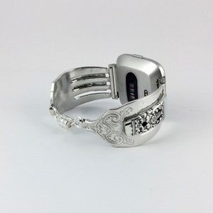 May include: Silver smartwatch band made from a repurposed fork with an ornate design. The band is attached to a silver smartwatch with a black screen.