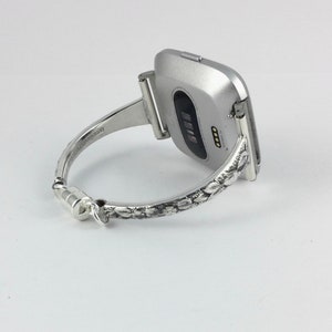 May include: A silver bracelet with a floral design that holds a silver smartwatch.