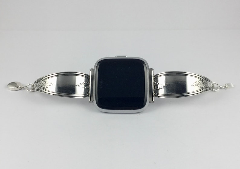 May include: A silver smartwatch with a black screen is attached to a silver spoon band. The band is made from two spoons that have been bent into a loop and attached to the watch.
