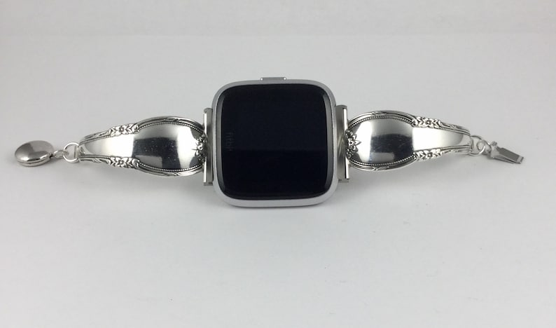 May include: A silver smartwatch with a black screen is attached to a silver bracelet made from two spoons. The bracelet has a decorative design and a clasp.