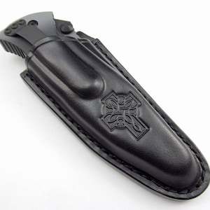 Peut inclure: Étui à couteau en cuir noir avec un motif de nœud celtique en relief sur le devant. L'étui a un bord cousu et un rabat qui se ferme à l'aide d'un bouton-pression.
