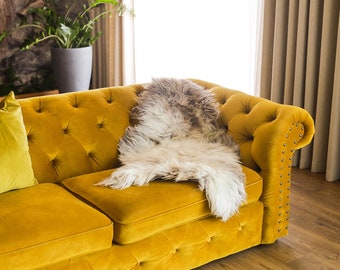 May include: A mustard yellow velvet sofa with tufted buttons and nailhead trim. A white sheepskin throw is draped over the sofa.