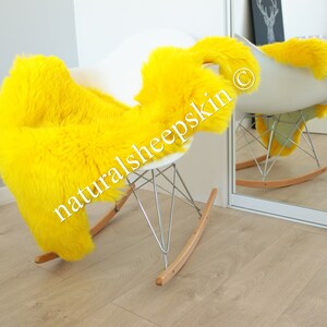 May include: A bright yellow sheepskin rug draped over a white rocking chair. The chair has a chrome frame and wooden rockers. The rug is labeled "naturalsheepskin" in the image.
