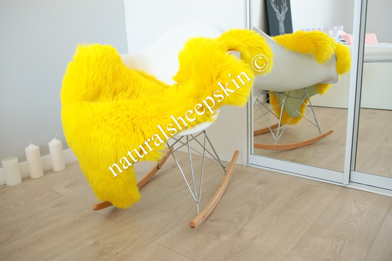 May include: A bright yellow sheepskin rug draped over a white rocking chair. The chair has a chrome frame and wooden rockers. The rug is labeled "naturalsheepskin" in the image.