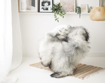 May include: A large, fluffy, faux fur rug in shades of gray and white sits on a small, striped rug. The rug is the focal point of a bright, minimalist room with framed artwork and a woven pendant light.