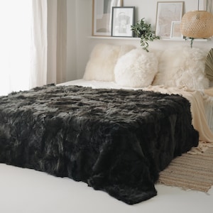 Könnte beinhalten: Eine kuschelige schwarze Kunstfell-Decke auf einem Bett mit weißen Kissen. Die Decke ist weich und flauschig und perfekt, um jedem Raum Wärme und Gemütlichkeit zu verleihen.