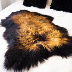 May include: A black and brown sheepskin rug with long, soft fur. The rug is laid out on a white bedspread.
