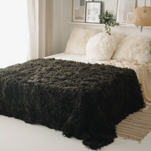 Könnte beinhalten: Eine dunkelbraune, flauschige Wolldecke auf einem Bett mit weißen Kissen und einem beigefarbenen Teppich.